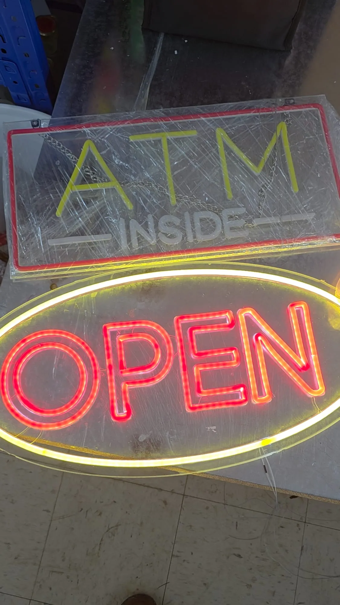 Red OPEN lit inside a yellow oval and a yellow ATM INSIDE sign wrapped in clear plastic, side by side on a workbench.
