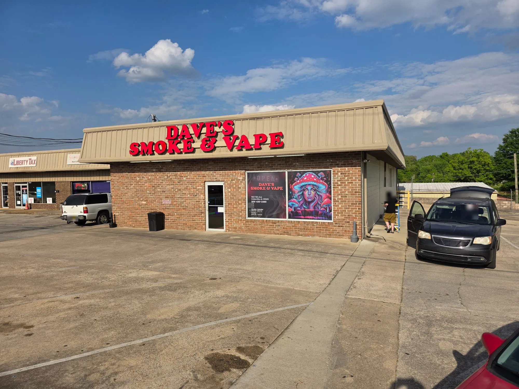 Angled view of a brick storefront with glossy red raised letters on a tan metal band, a glass door and a printed poster in the window.