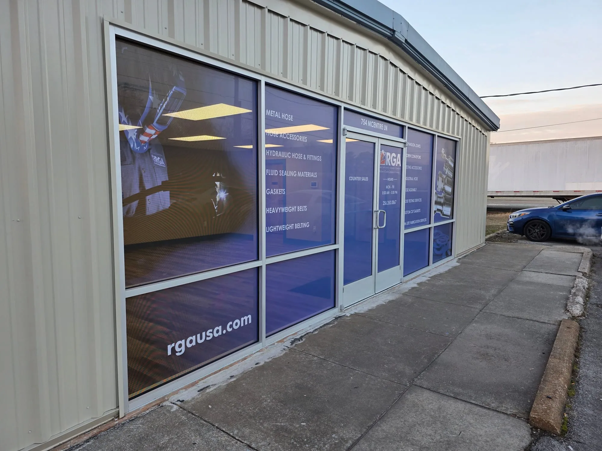 Angled view along the front of the same building, showing the printed product list in white text and a large photo of chrome fittings on the right-hand windows.