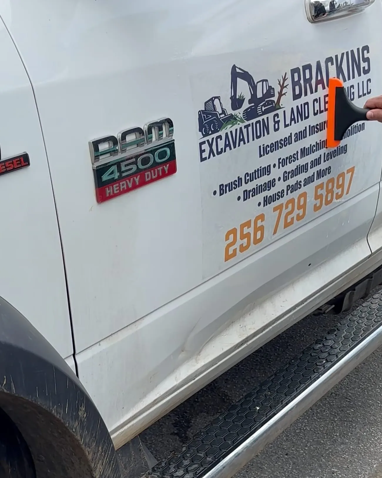 A hand pressing an orange squeegee across the printed door graphic on a white pickup door.
